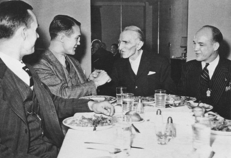 Nikola Tesla having a discussion at a dinner table. 